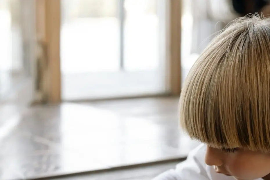 A young boy counting coins and placing them into a jar labeled 'for barbie castle' indoors on wooden flooring.